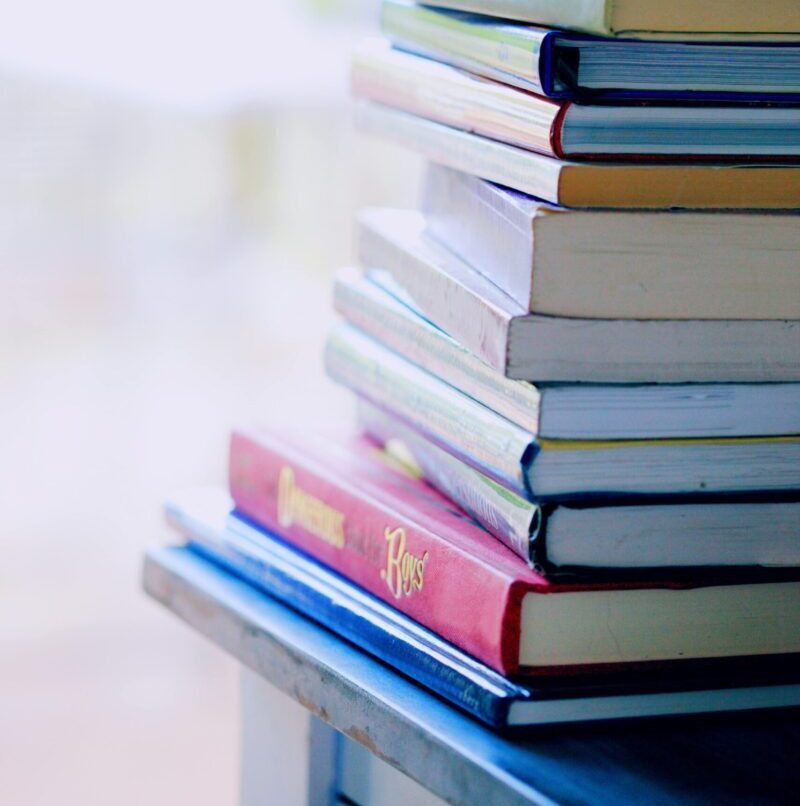 A tall stack of colorful hardcover books on a table indoors, perfect for library-themed concepts.