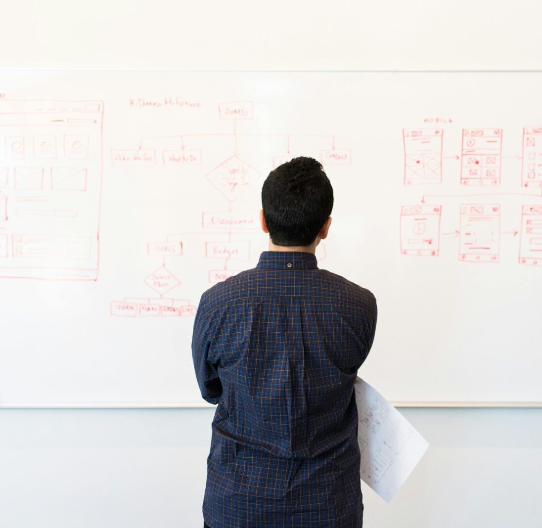 Man analyzing design flowchart on whiteboard in a professional office setting.